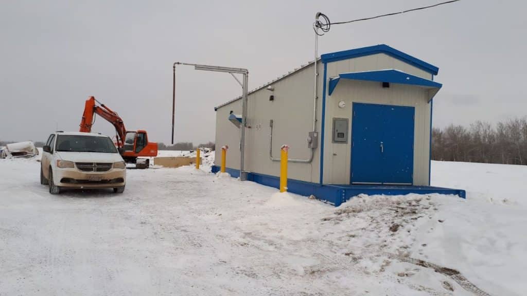 A picture of a water station with a white van next to it and a piece of heavy equipment in the background in the winter.