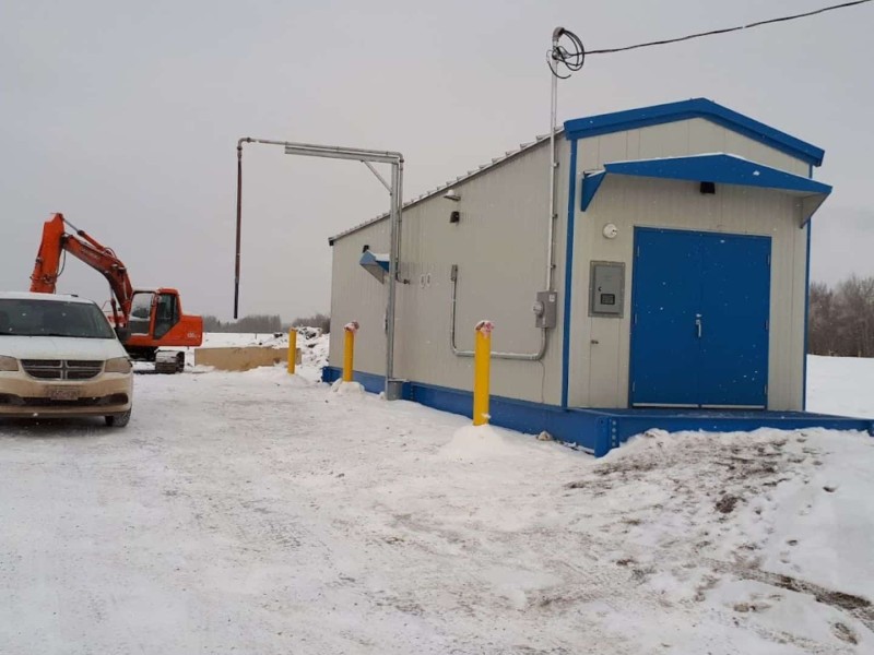 A picture of a water station with a white van next to it and a piece of heavy equipment in the background in the winter.