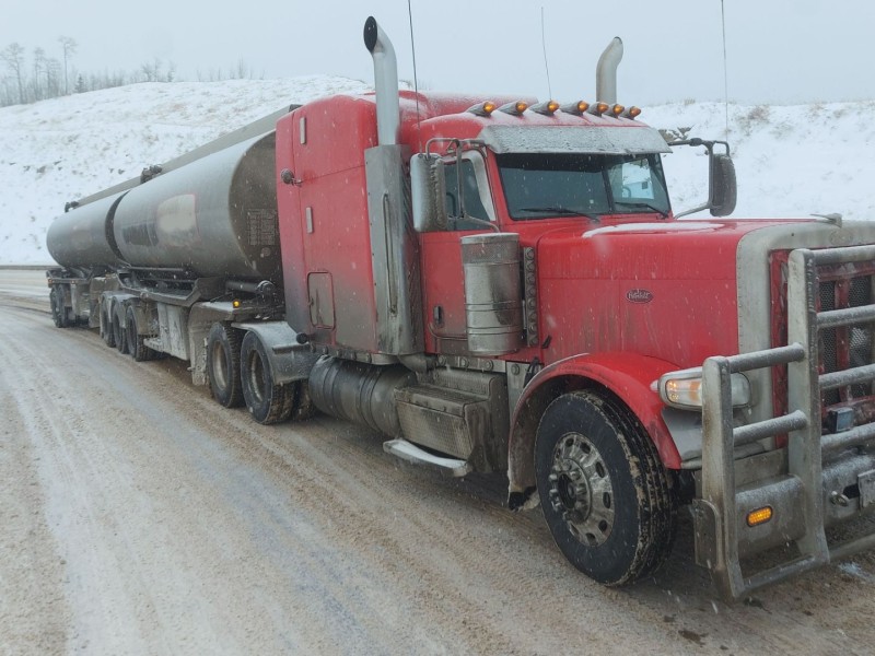 A red and silver semi-truck drives up the South Taylor Hill in the winter.