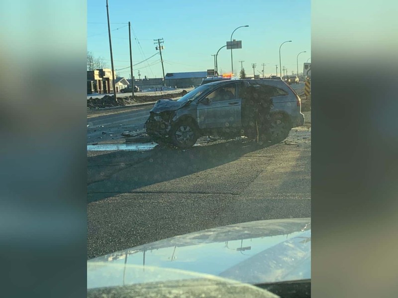 A photo of a SUV with the front end crushed with a person looking into the drivers door on the Alaska Highway.