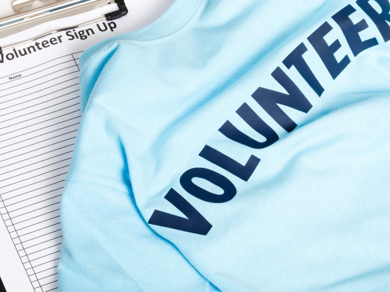 A blue shirt that reads 'Volunteer' atop a sign up sheet for volunteers.