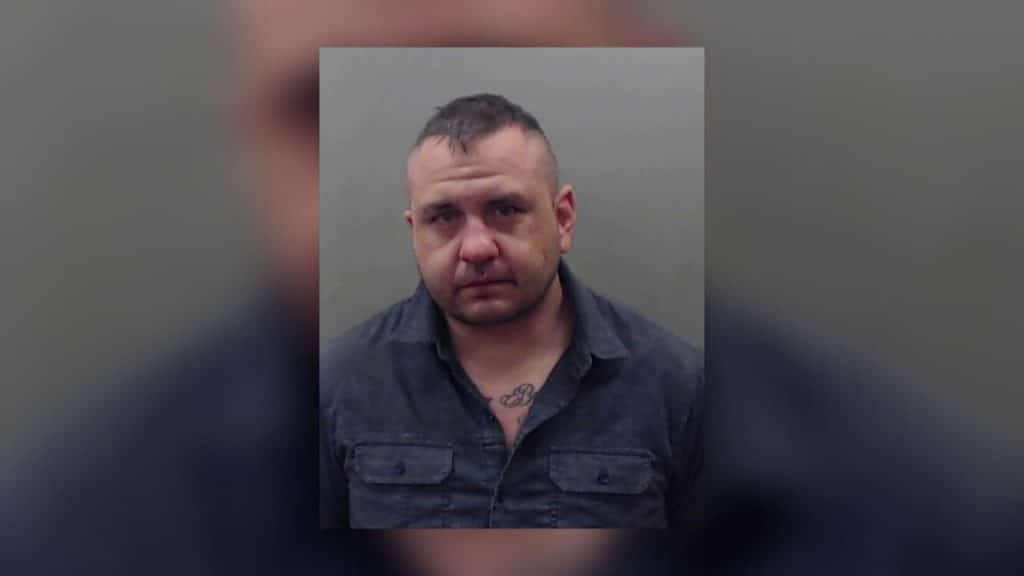 A photo of a man named Joel Dustin Toth, wearing a blue shirt on a grey background. 