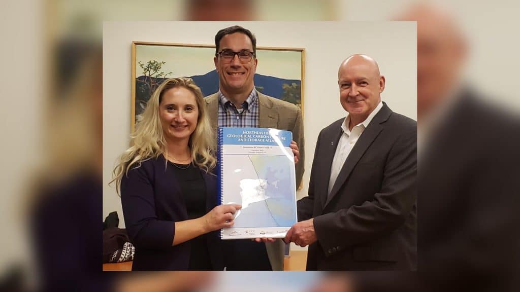 A trio of people, one woman and two men, hold an atlas on carbon storage capture.