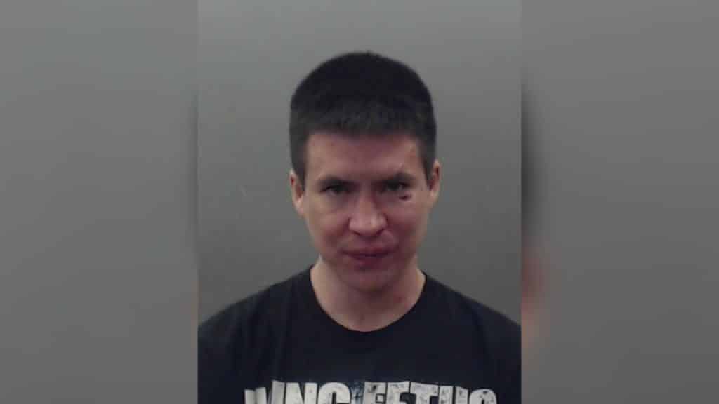 A picture of a short, brown haired man standing in front of a grey background.