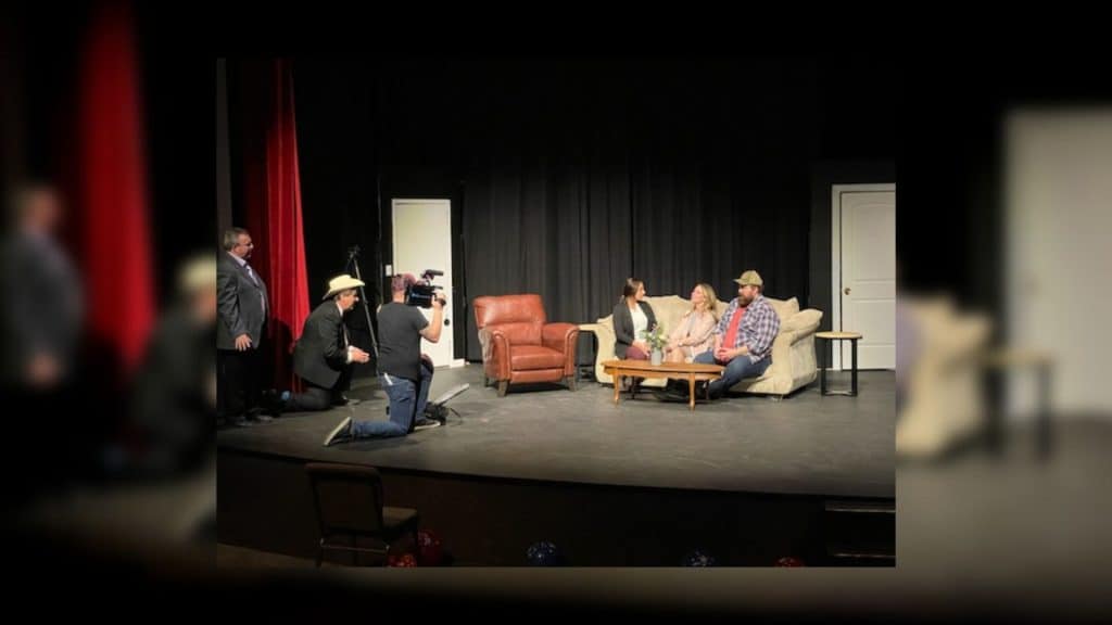Actors on a stage sitting on a couch.