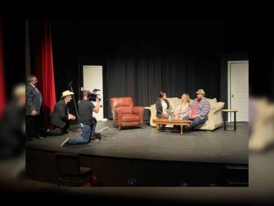 Actors on a stage sitting on a couch.
