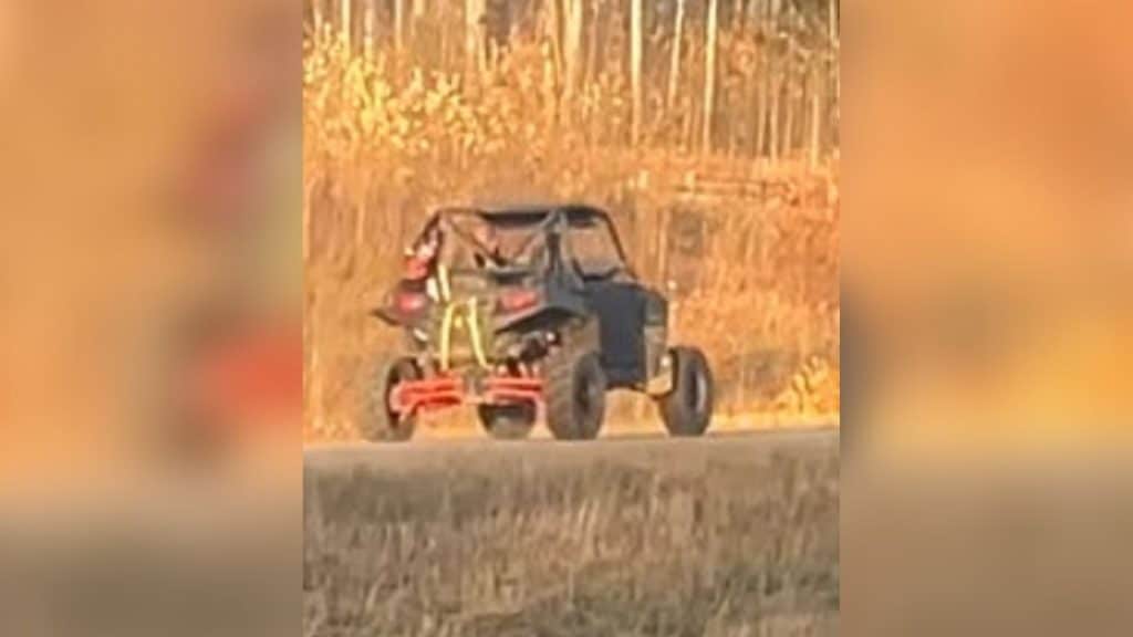 A picture of a UTV driving away from the photographer in the fall, dead grass in the foreground and bare trees in the background.