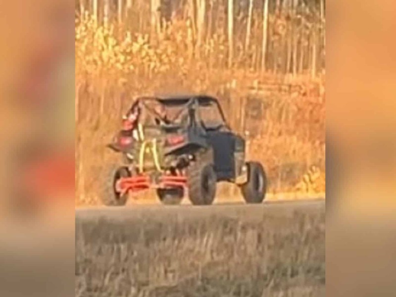A picture of a UTV driving away from the photographer in the fall, dead grass in the foreground and bare trees in the background.