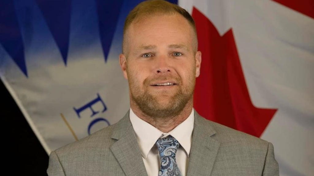 A middle-aged man with a beard wearing a grey suit.