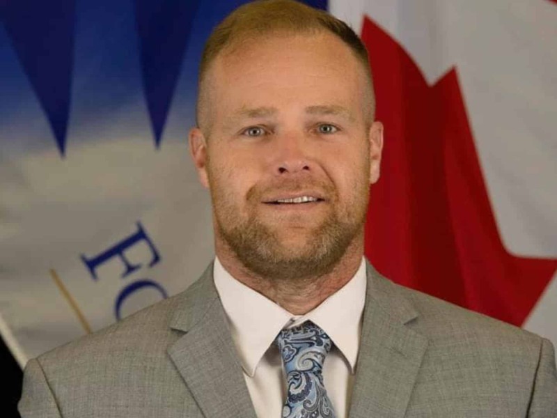 A middle-aged man with a beard wearing a grey suit.
