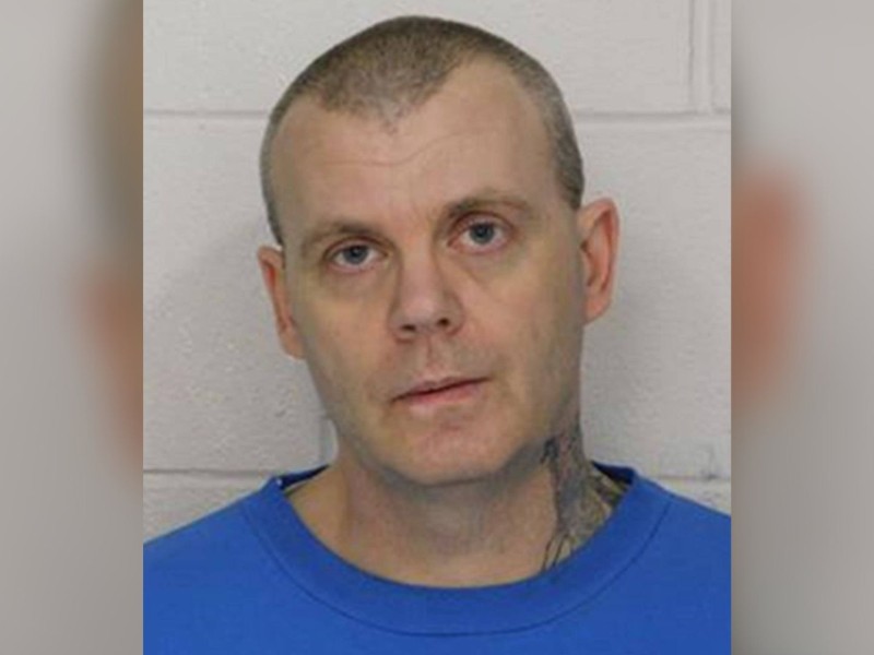 A man in a blue shirt in front of a white wall.