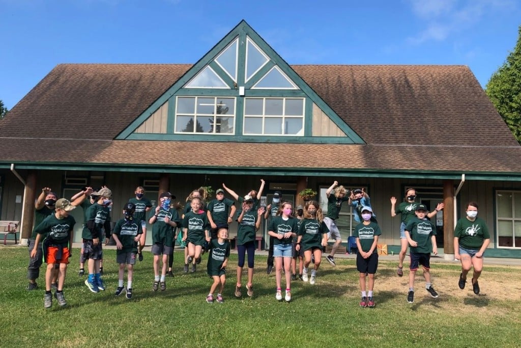 A group of kids in green shirts jumping and posing in front of a building.