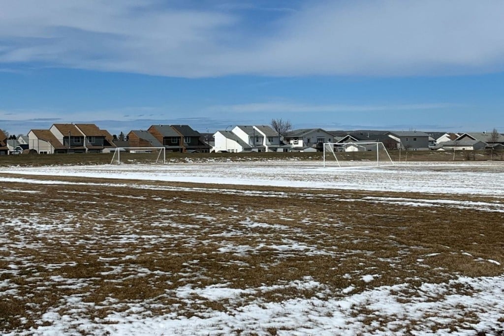 A field with some snow on it with some houses in the background.