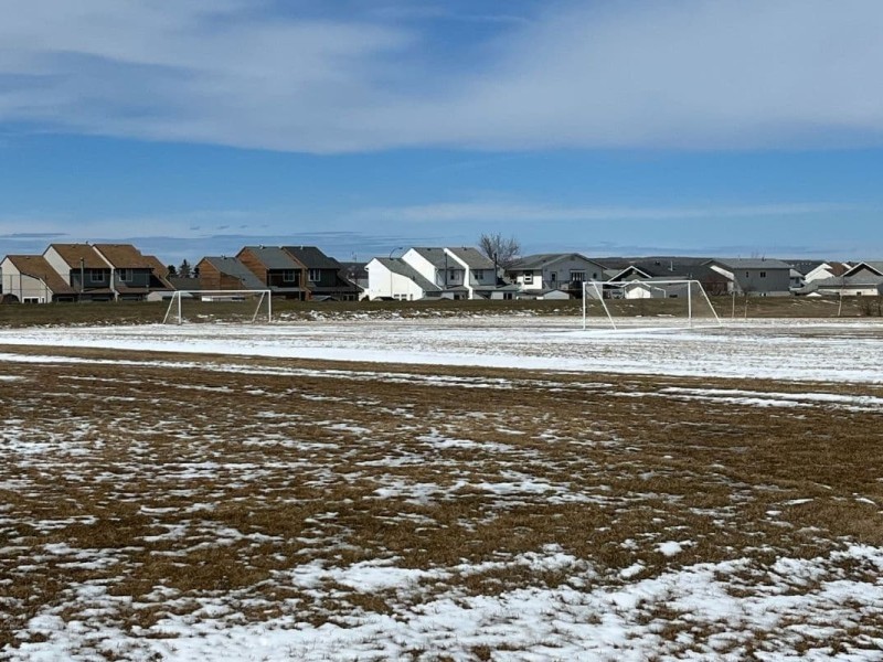 A field with some snow on it with some houses in the background.
