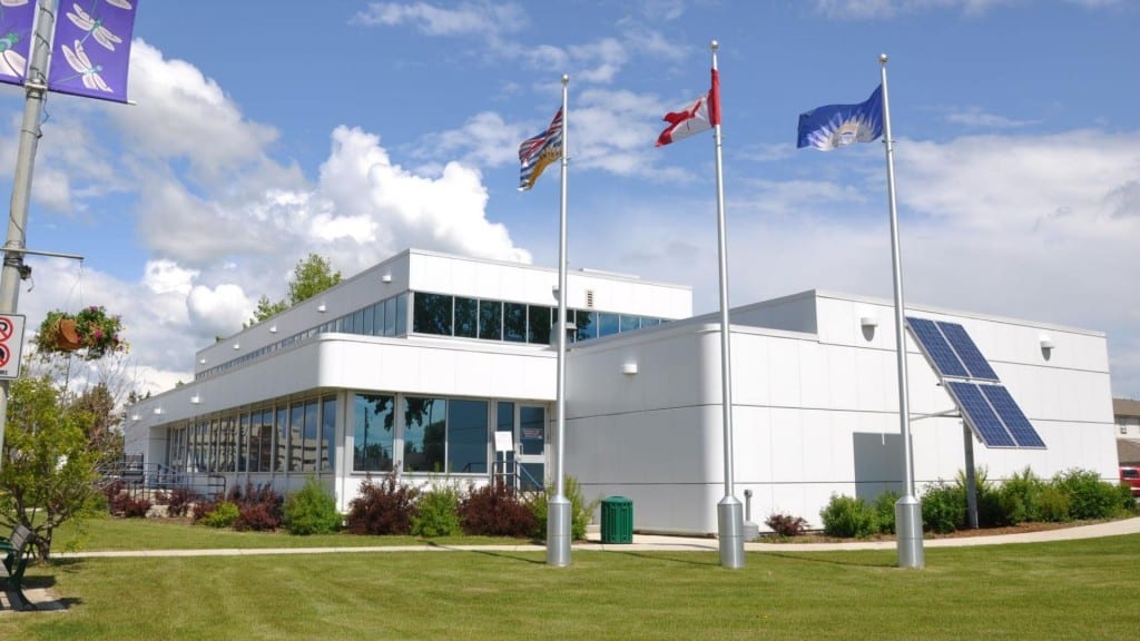 Fort St. John City Hall. A large white building with three flag poles and flags in front of it.