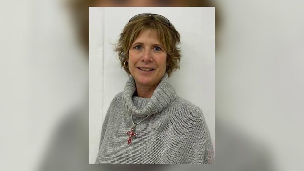 A woman with ear length brown hair in a grey sweater.