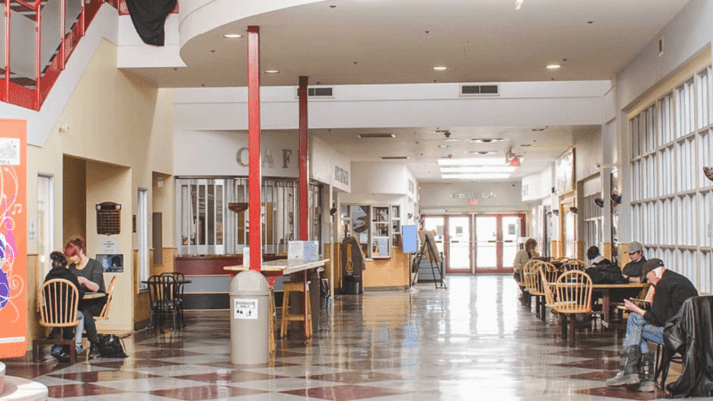 The inside of a building with people sitting on chairs at tables on a tile floor.