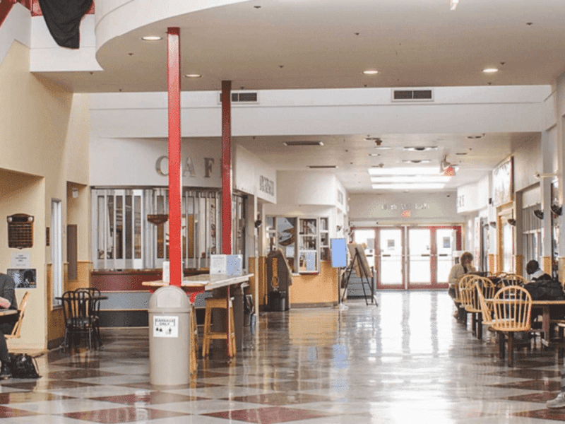 The inside of a building with people sitting on chairs at tables on a tile floor.