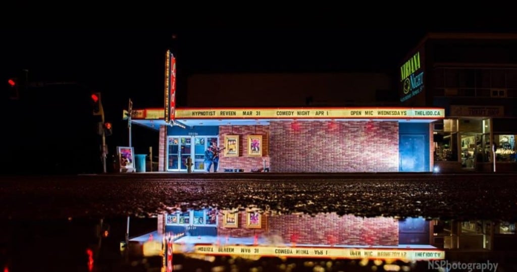 A picture of Fort St. John's Lido Theatre front entrance lit up on a dark night, with a reflection of the brick building in a puddle.
