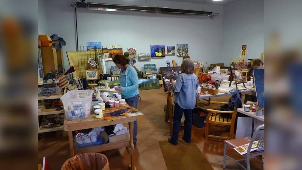 A small group of people working on art in an art studio with art on the walls, multiple areas to work and art supplies everywhere.