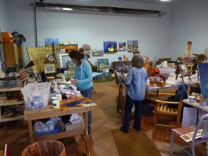 A small group of people working on art in an art studio with art on the walls, multiple areas to work and art supplies everywhere.
