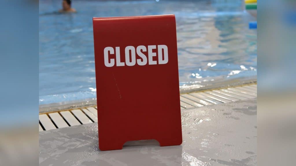 A red closed sign in front of a pubic pool.