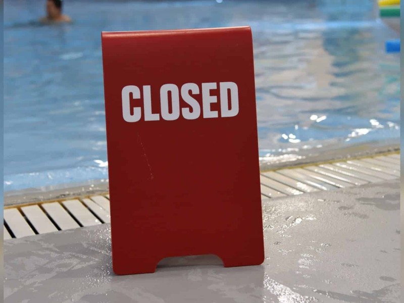 A red closed sign in front of a pubic pool.