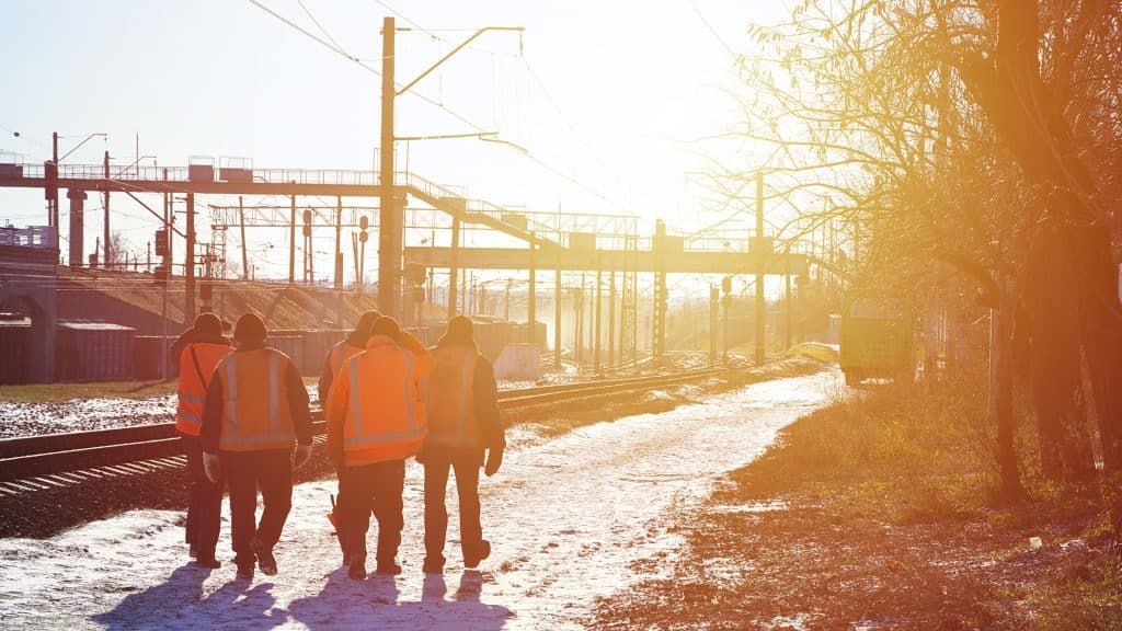Men walking away from the camera in high visible jackets and vests in the snow.