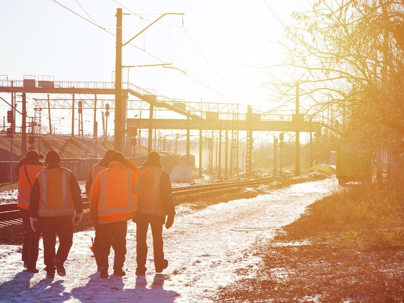 Men walking away from the camera in high visible jackets and vests in the snow.