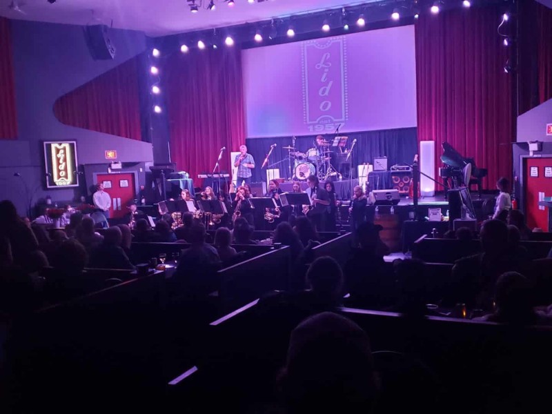 A purple lit theatre where a high school band is performing.
