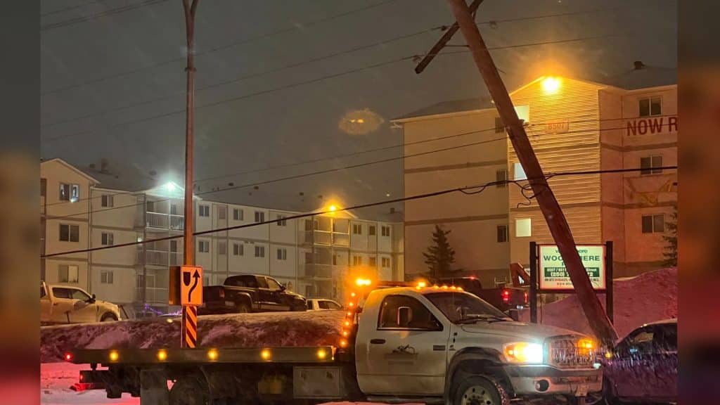 A powerline knocked at an angle at night. A white truck is parked beneath it.