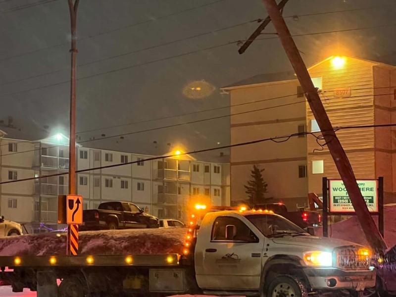 A powerline knocked at an angle at night. A white truck is parked beneath it.