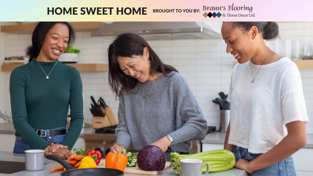 Three people standing in kitchen. Person on left smiling, person in middle cutting vegetables, person on right smiling