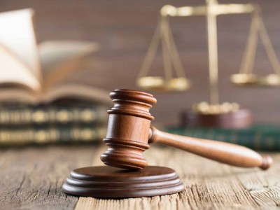 A justice's gavel on a wooden surface in front of books and scales.