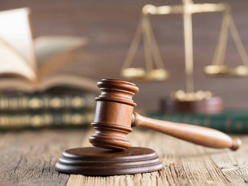 A justice's gavel on a wooden surface in front of books and scales.