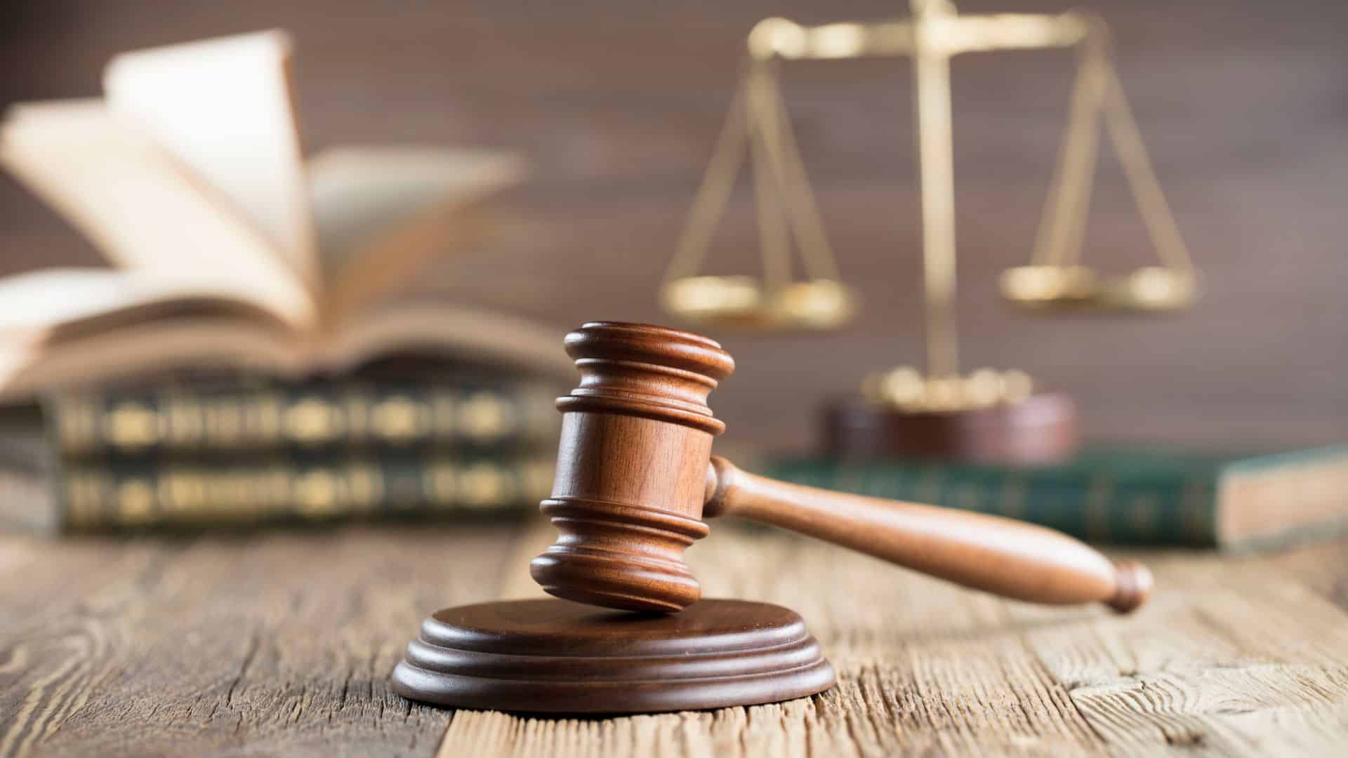 A justice's gavel on a wooden surface in front of books and scales.