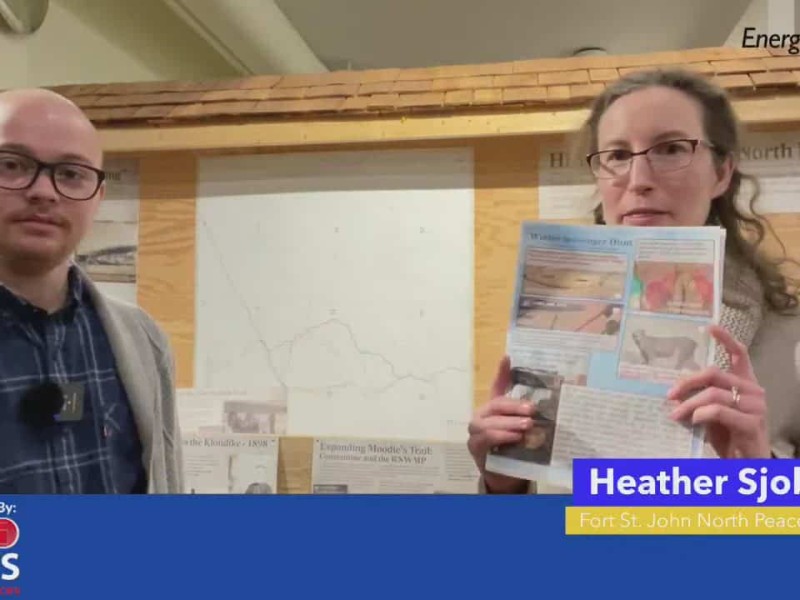 Person on left in plaid shirt and sweater looking at camera. Person on right holding up a scavenger hunt checklist