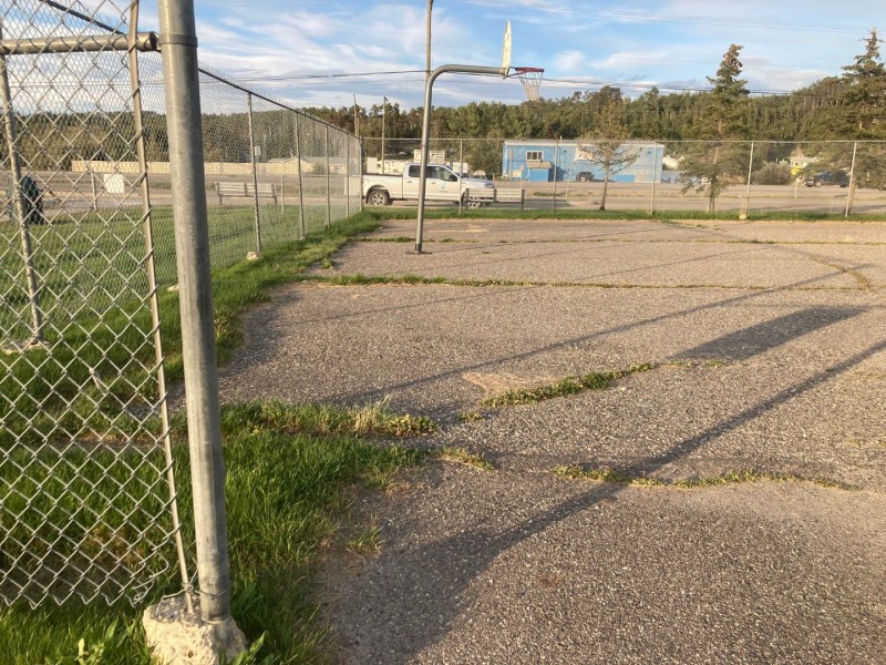 An old, asphalt basketball court surrounded by a chain-link fence and gross.