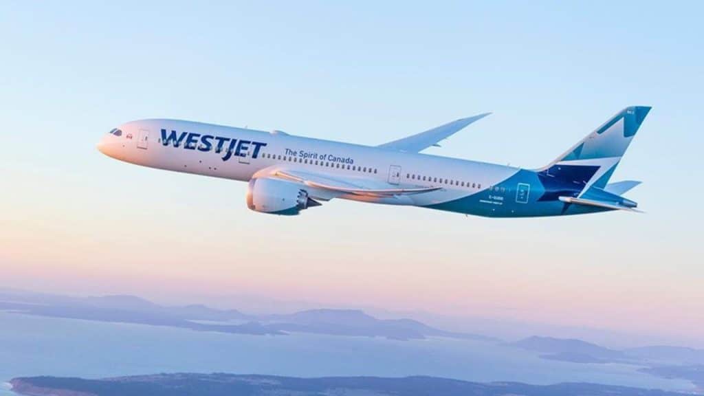 A WestJet aircraft in the sky, with a body of water and land seen in the background.