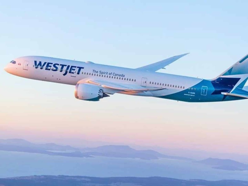 A WestJet aircraft in the sky, with a body of water and land seen in the background.