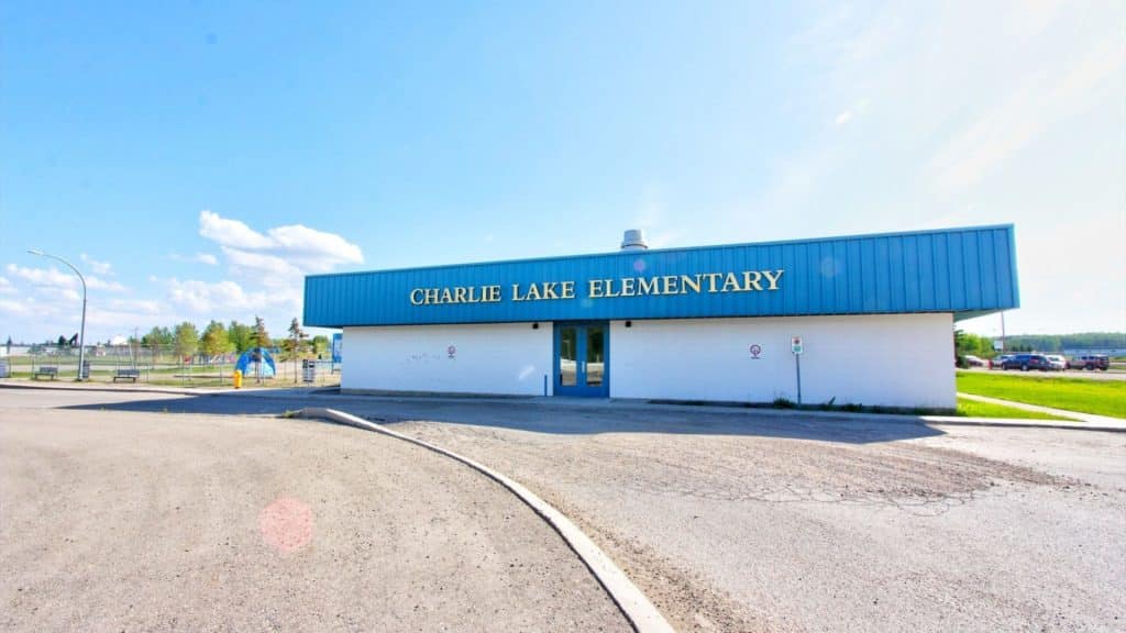 A picture of the Charlie Lake Elementary school, a blue and white building with a playground in the background.