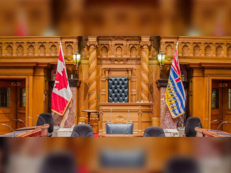 A wood paneled room with a Canadian and BC flag on either side of a black, leather seat.