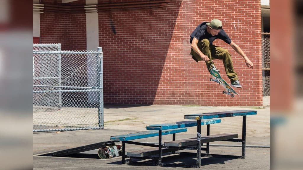 A man in a t-shirt doing a skateboard trick above a set of blue benches.
