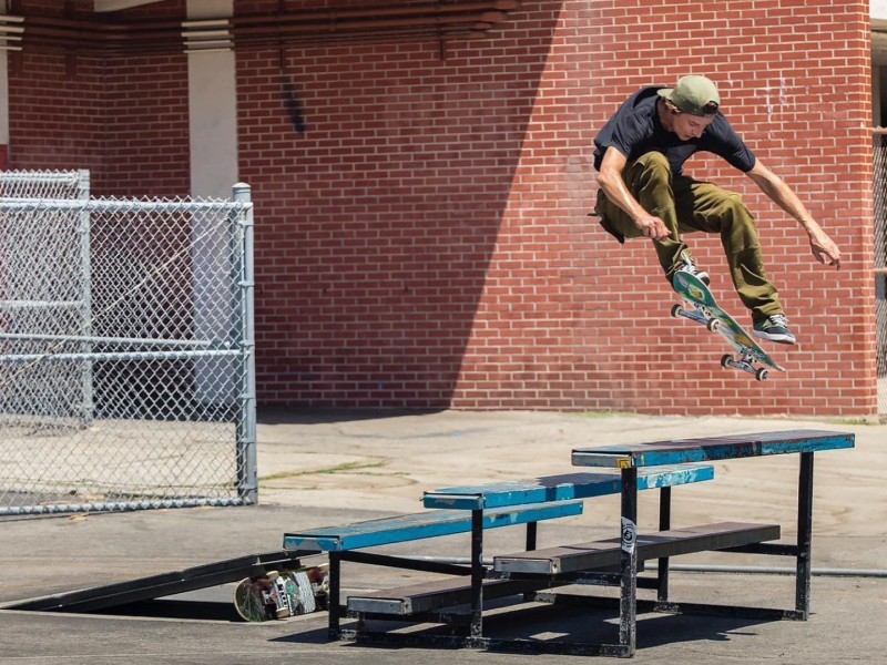 A man in a t-shirt doing a skateboard trick above a set of blue benches.