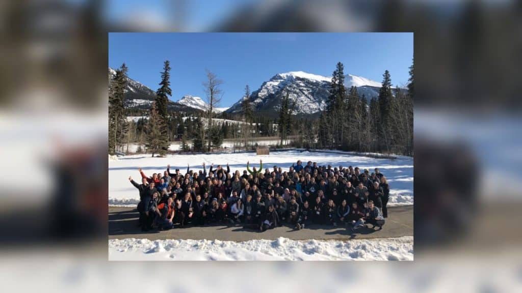 A large group of students in Canmore, Alberta in a snowy park with trees and mountains in the background.