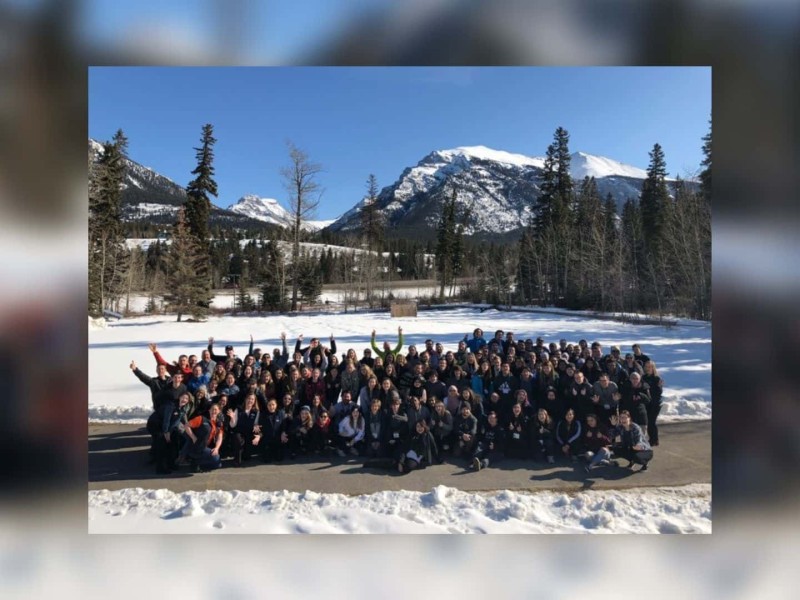 A large group of students in Canmore, Alberta in a snowy park with trees and mountains in the background.