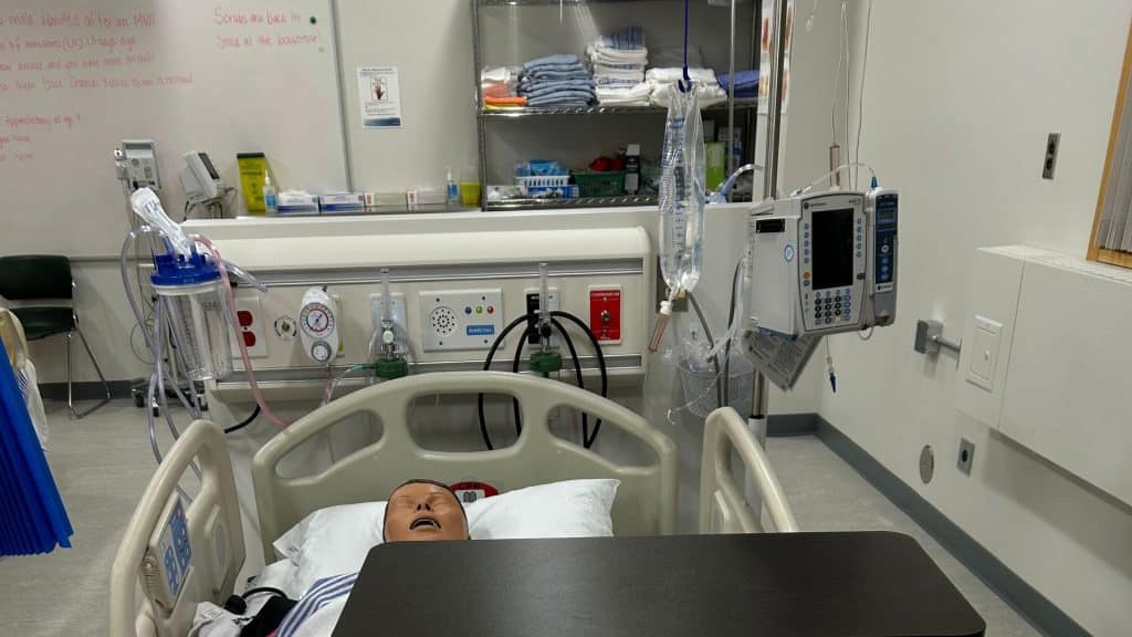 A lab set up for students in the Northern Baccalaureate Nursing program with a dummy in a bed and a whiteboard in the background.