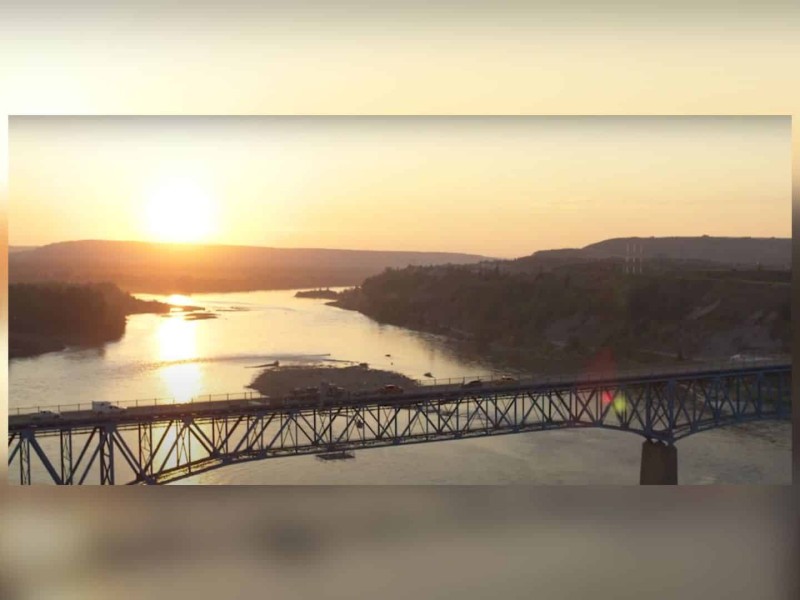 A screenshot of the Taylor Bridge with vehicles on it and a sunset/rise in the background.
