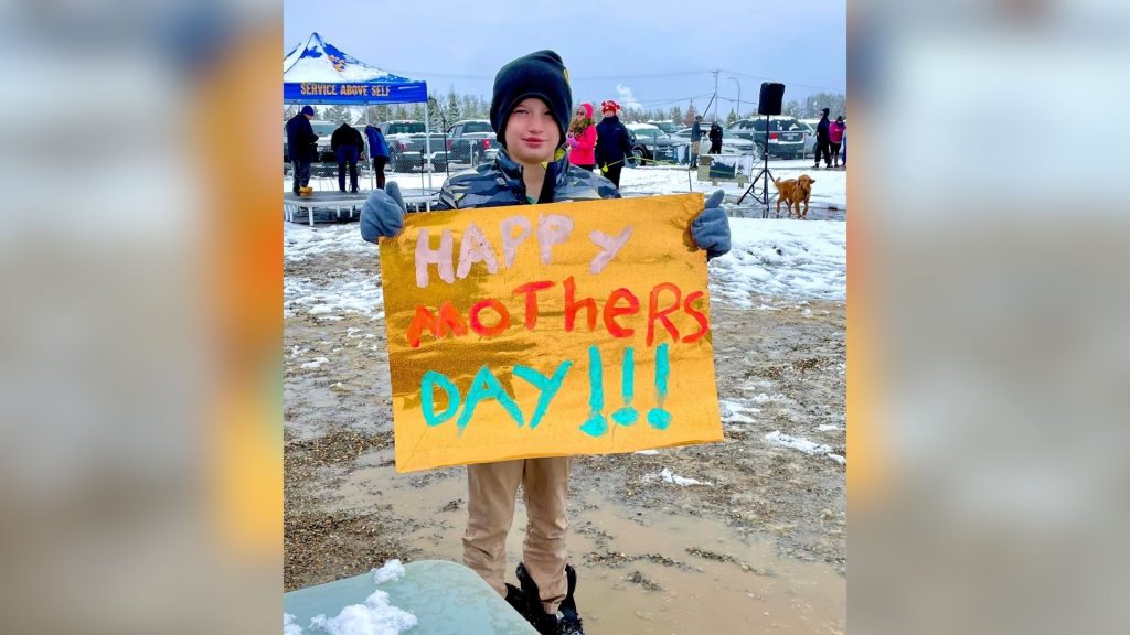 A child holding a sign Happy Mothers Day sign in the snow.