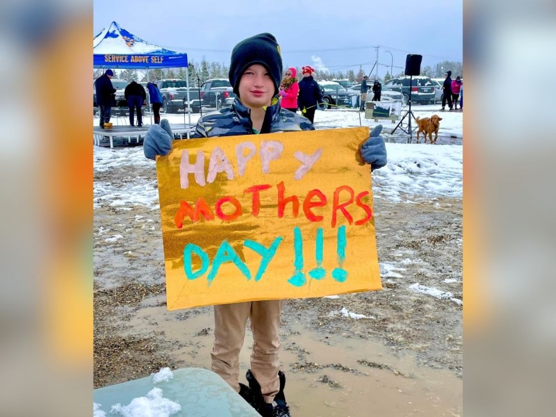 A child holding a sign Happy Mothers Day sign in the snow.